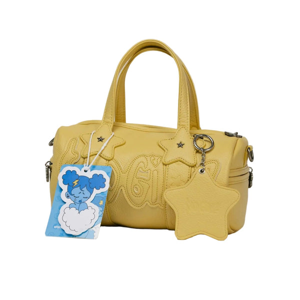 A yellow faux-leather handbag with embossed lettering, featuring a star-shaped keychain charm and a blue cartoon tag, photographed on a light gray background.
